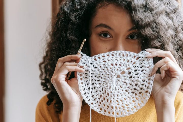 African American female with dark wavy hair wearing yellow pullover covering up mouth with white napkin with crochet and thread